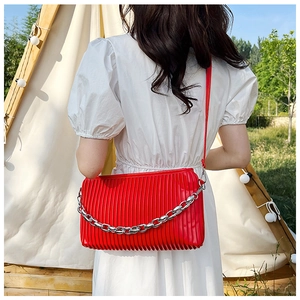 Fashionable red pleated shoulder bag with silver chain worn by model outdoors
