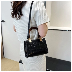 Close-up of black glossy crocodile pattern handbag with amber resin handle and metal clasp