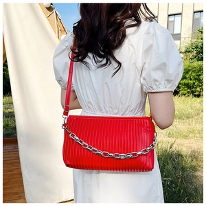 Detail of red pleated shoulder bag featuring a modern silver chain and faux leather texture