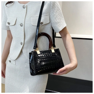 Close-up of black glossy crocodile pattern handbag with dark brown handles and gold hardware