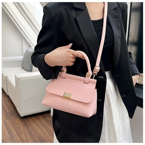 Detail of light pink lychee texture bag with gold clasp on a model in a black blazer