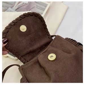 Detail of magnetic gold clasp and braided suede texture on a brown fringe saddle bag