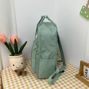 Close-up of mint green canvas backpack featuring side pocket and durable woven handle strap