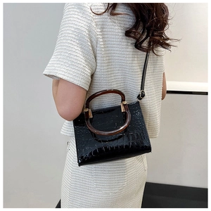 Detail of black glossy crocodile pattern tote with amber handles worn by a model