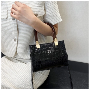 Detail of black crocodile texture handbag with amber resin handle and gold metal links
