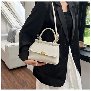 Close-up of beige lychee grain leather handbag with golden lock and strap details