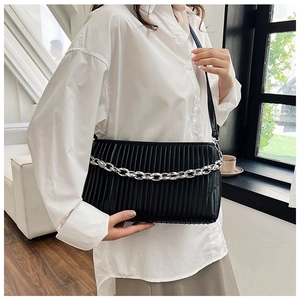Detail of a black pleated shoulder bag featuring a chunky silver chain on a model
