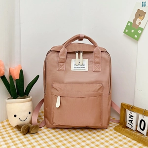 Close-up of pink college backpack with double handles and logo label on checkered table