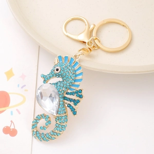 Golden seahorse keychain pendant with blue rhinestones on a white ceramic plate