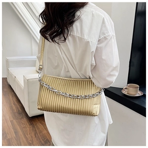 Detail of golden pleated shoulder bag with chunky silver chain on white shirt