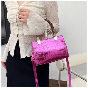 Detail of glossy fuchsia crocodile pattern handbag with amber handle and metallic finish