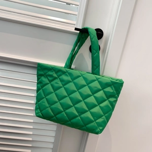 Bright green quilted tote bag with wide handles and glossy finish in minimalist setting