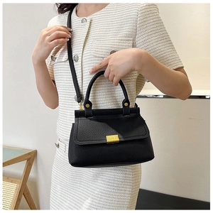 Close-up of black lychee grain leather handbag with gold metal clasp on model