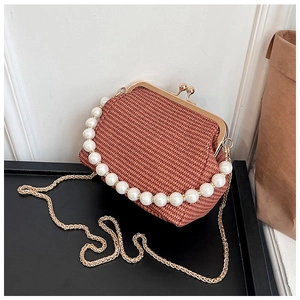 Détail du sac à clip tissé avec poignée en perles et chaîne dorée sur plateau