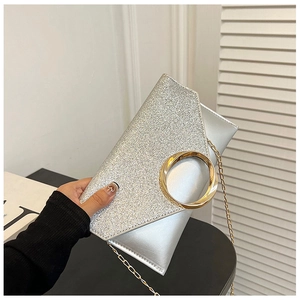 Close-up of sparkling silver glitter envelope clutch with gold round handle and chain strap