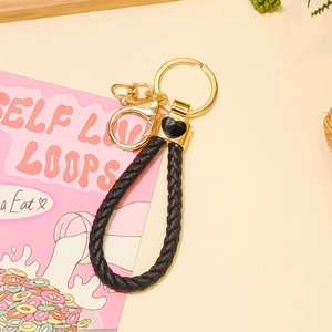 Détail du porte-clés en cuir tressé noir avec fermoir doré et élément de cœur