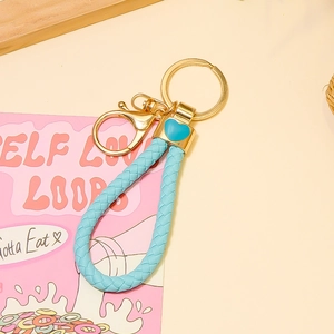 Gros plan d'un porte-clés en cuir tressé bleu clair avec fermoir doré et pendentif cœur
