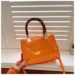 Detailed close-up of glossy orange faux leather handbag with crocodile pattern and amber handles