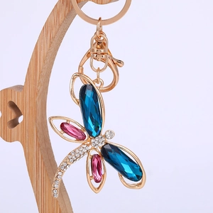 Exquisite dragonfly keychain with blue gemstones and sparkling crystals on a wooden stand