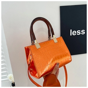 Detail view of glossy orange faux crocodile leather handbag with resin handle and strap