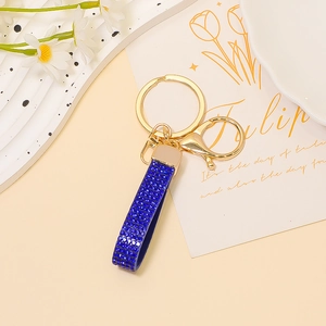 Dettaglio portachiavi in pelle blu reale con strass, anello dorato e chiusura a moschettone