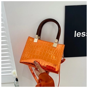 Detail of orange faux crocodile leather handbag with resin handle and shiny finish