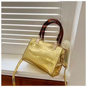 Detail of glossy gold crocodile pattern handbag with resin tortoiseshell ring handle