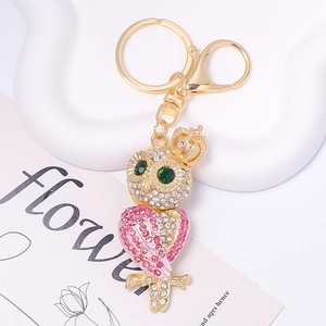 Close-up of gold owl keychain with pink rhinestones and crown detail on white tray