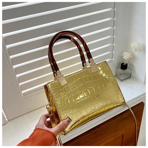 Detail of glossy gold crocodile pattern handbag with amber handles and metal hardware