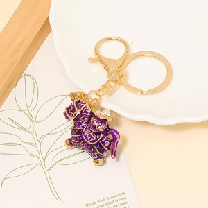Detailed view of a purple enamel horse keychain with gold patterns and pearl on a white plate