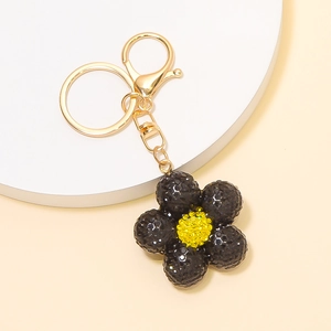 Vue macro d'un porte-clés fleur noire avec strass jaune sur un support blanc élégant