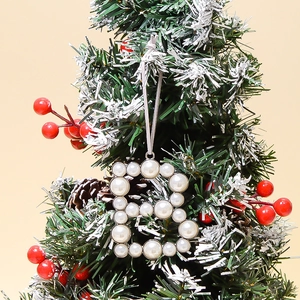 Detail of pearl-beaded letter B ornament hanging on a festive snowy Christmas tree branch