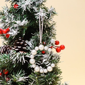 Close-up of pearl wreath ornament with ribbon hanging on a snowy Christmas tree branch