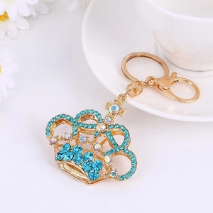 Sparkling gold crown keychain with light blue crystals and cross pendant on white background