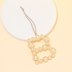 Close-up of golden letter B pendant charm featuring embedded white pearls and grey cord