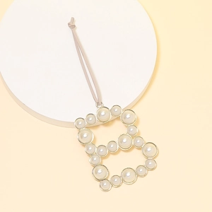 Detail view of pearl-inlaid letter B pendant with golden metal frame and grey string