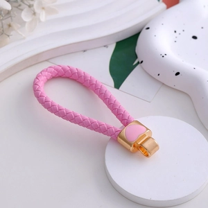 Detailed close-up of a pink woven leather keychain with a golden heart charm on a tray