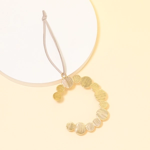 Detail of golden textured circular alphabet charm with ribbed metal surface and grey strap