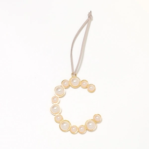 Macro detail of gold letter C keychain charm with white inlaid pearls and a grey lanyard
