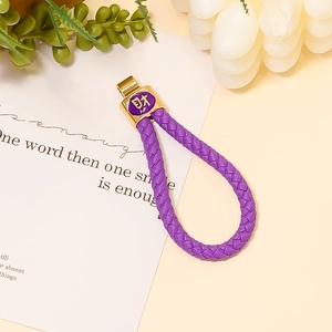Dettaglio portachiavi in pelle intrecciata viola con ciondolo dorato e simbolo Cai