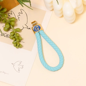 Dettaglio del portachiavi in pelle intrecciata azzurra con ciondolo dorato Fu