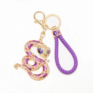 Détail d'un porte-clés serpent doré avec cristaux et cordon tressé de couleur violette