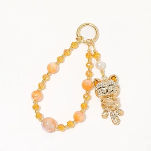 Gold cat keychain with sparkling crystals and orange beaded wrist strap on white background