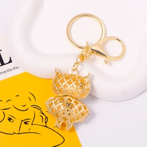 Golden owl keychain with hollow enamel craft and crystal accents on a display tray