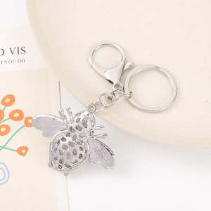 Detailed silver bee keychain with intricate wing texture and lobster clasp on a ceramic plate