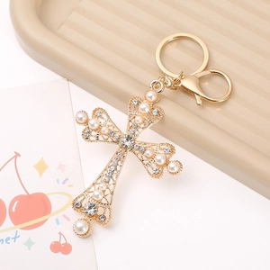 Elegant gold cross keychain with white pearls and sparkling rhinestones on textured surface