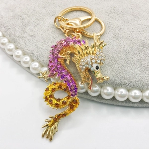Close-up of golden dragon keychain with purple and orange crystals on grey velvet