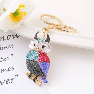 Porte-clés hibou coloré avec strass et fermoir doré sur un fond décoratif blanc