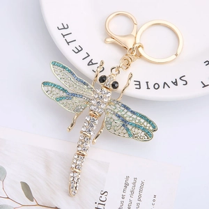 Golden dragonfly keychain with blue rhinestones and crystal wings on white dish