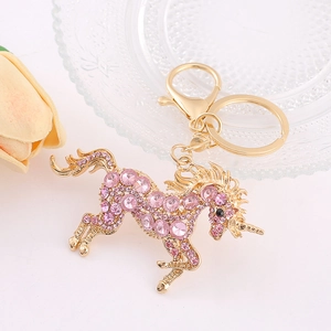 Porte-clés licorne doré orné de strass roses posé sur un plateau décoratif blanc